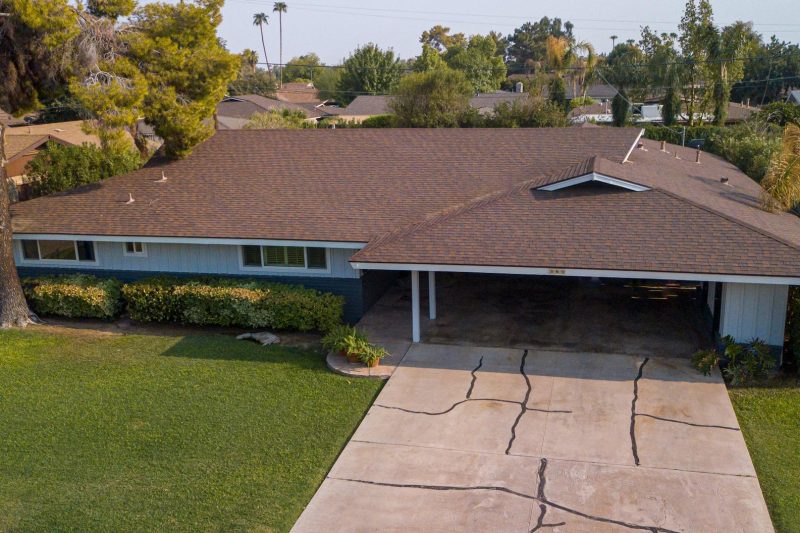 Aerial view of a suburban house with a brown roof, nestled among lush greenery.