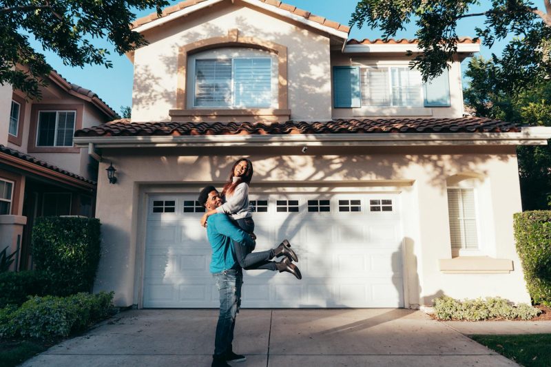 Joyful couple celebrating in front of their new house under a bright, sunny sky.