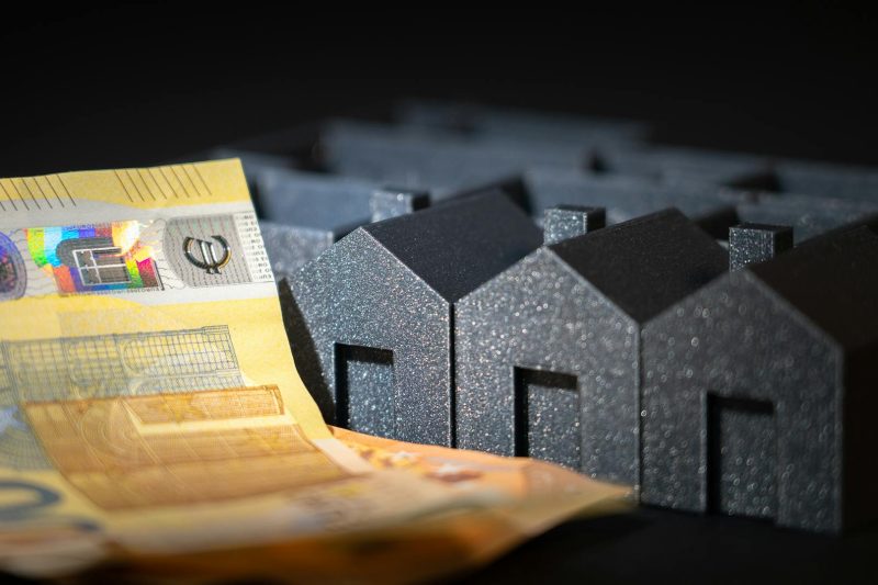 Black miniature houses surrounded by Euro notes, symbolizing investment in real estate and savings.