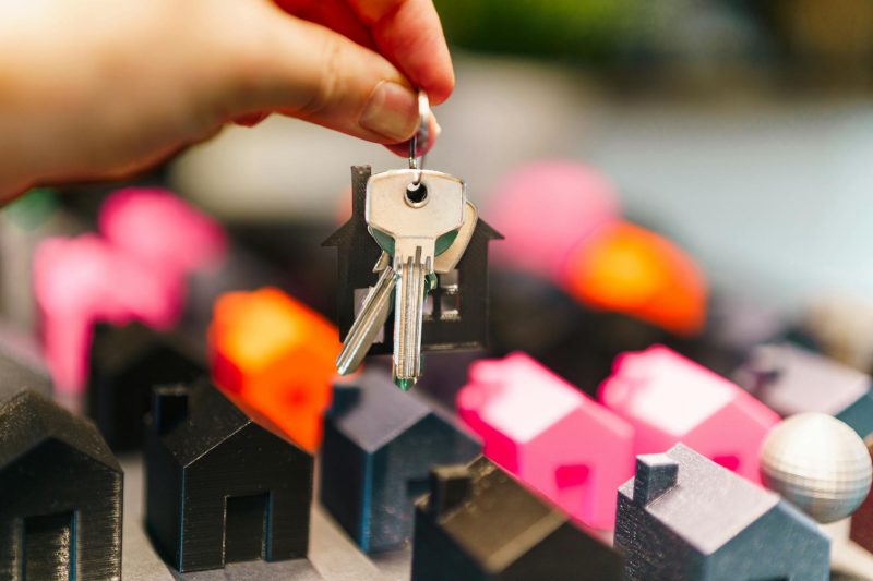 Colorful miniature houses with a hand holding a set of keys, symbolizing real estate ownership.