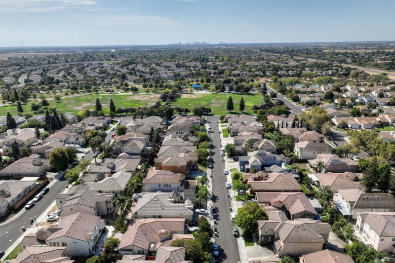 Aerial view of a Sacramento suburb showcasing neatly arranged houses surrounded by greenery under a clear blue sky.