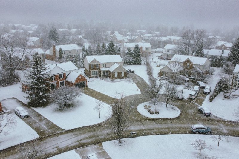 Aerial view of a snow-covered suburban neighborhood with quiet streets and neatly lined houses.